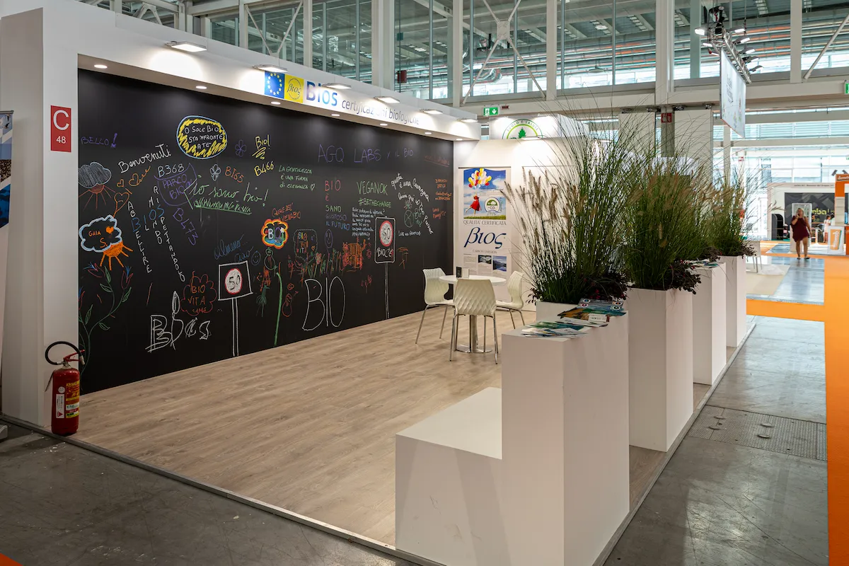 Fotografia dello stand Bios realizzato in fiera con parete nera coperta da scritte e disegni dei visitatori.