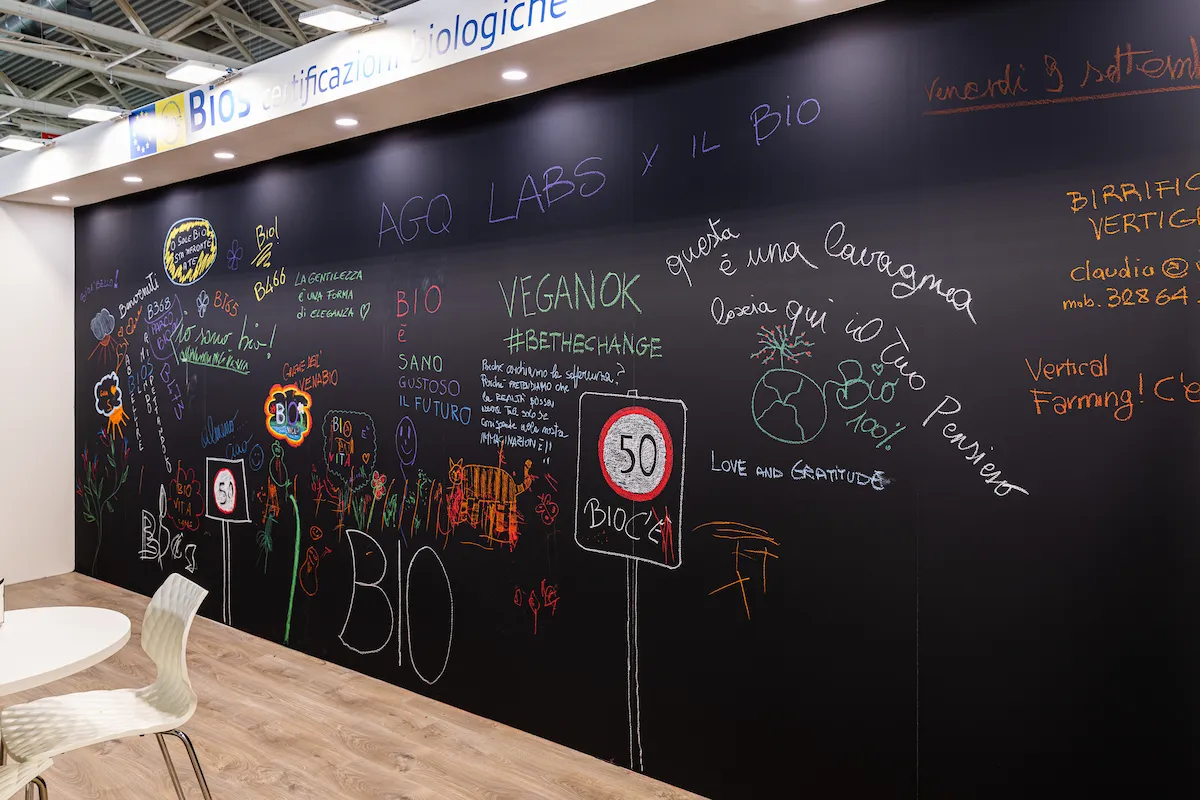 Primo piano della parete lavagna dello stand con messaggi colorati scritti a gesso sulla sostenibilità e il biologico.